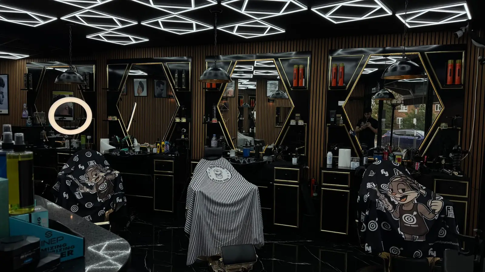 Barber stations with gold-framed hexagon mirrors under the LED ceiling